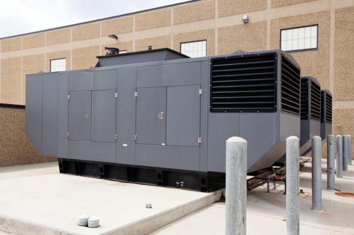 Three large industrial emergency power standby generators. This configuration could power a large facility such as a hospital, school even a small city. The concrete pad in the left foreground is space for an additional generator.