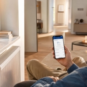 Heizung per App steuern mit Homematic – Homematic IP Heizkörperthermostat am Heizkörper im Wohnzimmer, Person steuert die Heizung per Smartphone-App