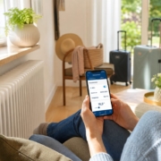 Heizung im Urlaub richtig einstellen: Energie sparen ohne Frostschäden Urlaubs- & Abwesenheitsmodus: Heizung clever einsparen – Frau mit Smartphone in der Hand stellt den Urlaubsmodus der Heizung ein, smarter Heizkörper-Regler an der Wand sichtbar